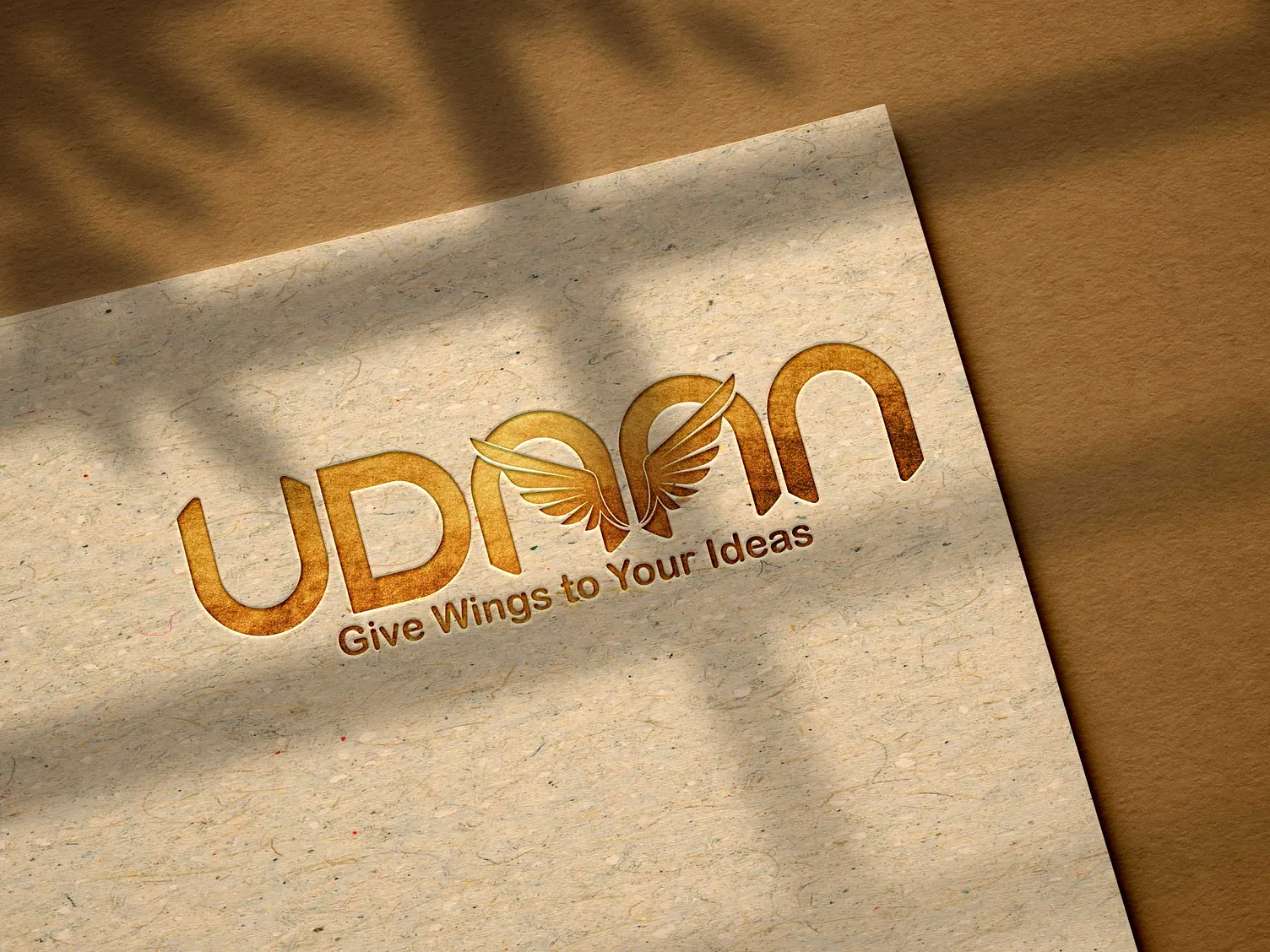 Udaan event logo — gold foil embossed lettering with wings in the A, on textured paper